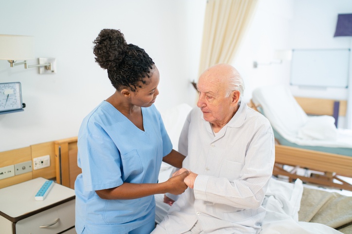 Nurse helping a senior man stand up from bed at long-term care facility in Bossier City
