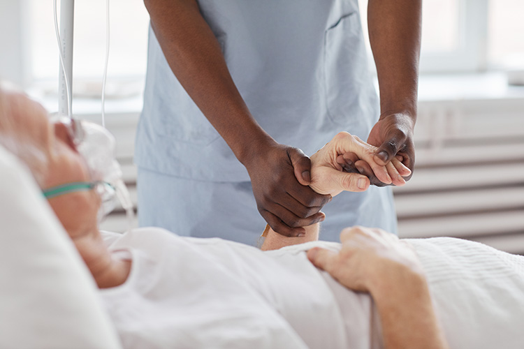 A hospice care nurse in Bossier City, LA holds a patient’s hand