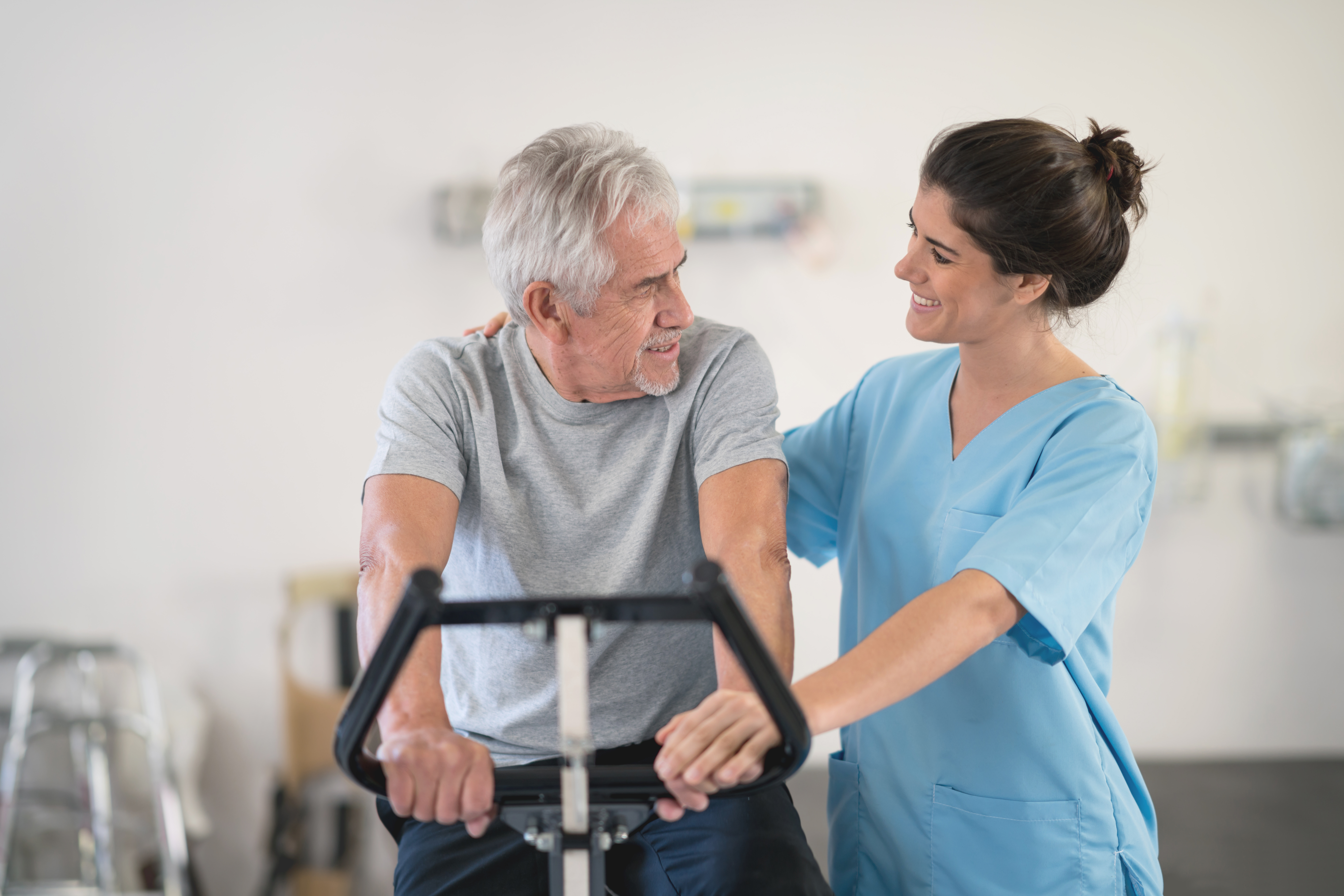 Physiotherapist motivating a senior man on a static bycicle looking at each other smiling