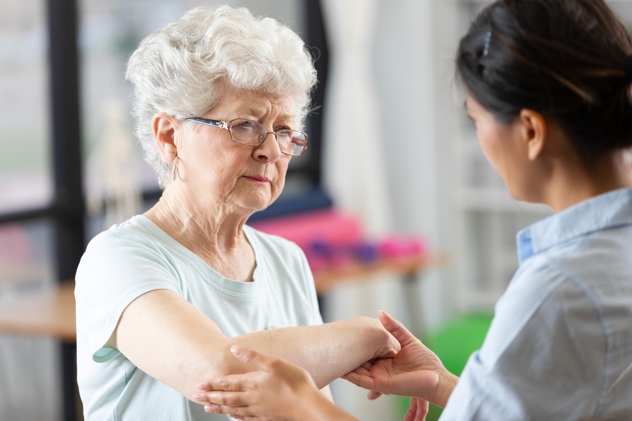 Doctor carefully examines senior patient's arm during medical examination indoors, demonstrating care and concern.