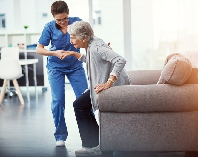 Nurse helping a senior patient up from a chair during short-term rehab