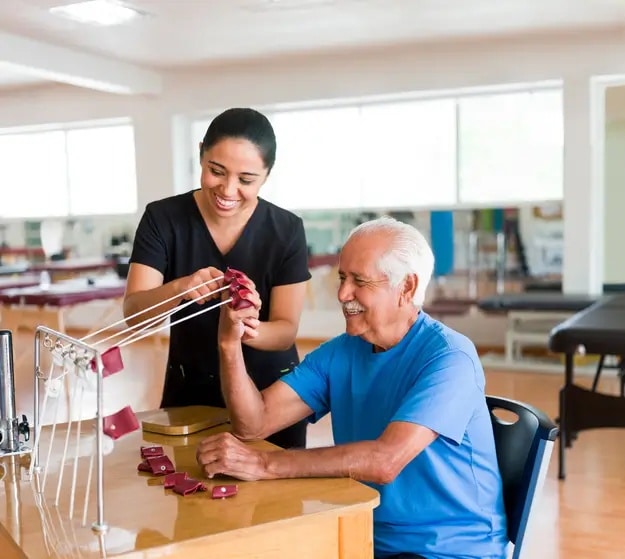 Senior man exercising his hand with a physical therapy device next to an occupational therapist