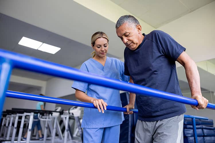 Senior man uses parallel bars during a physical therapy session with a therapist