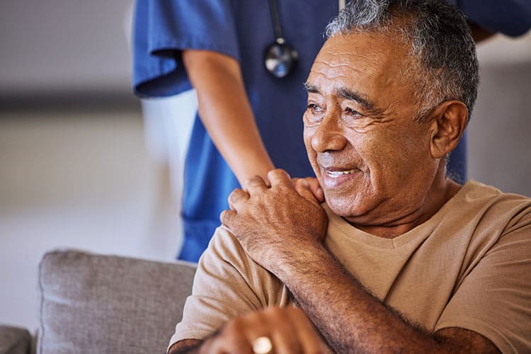 Senior man on a sofa greeted by a respite care nurse